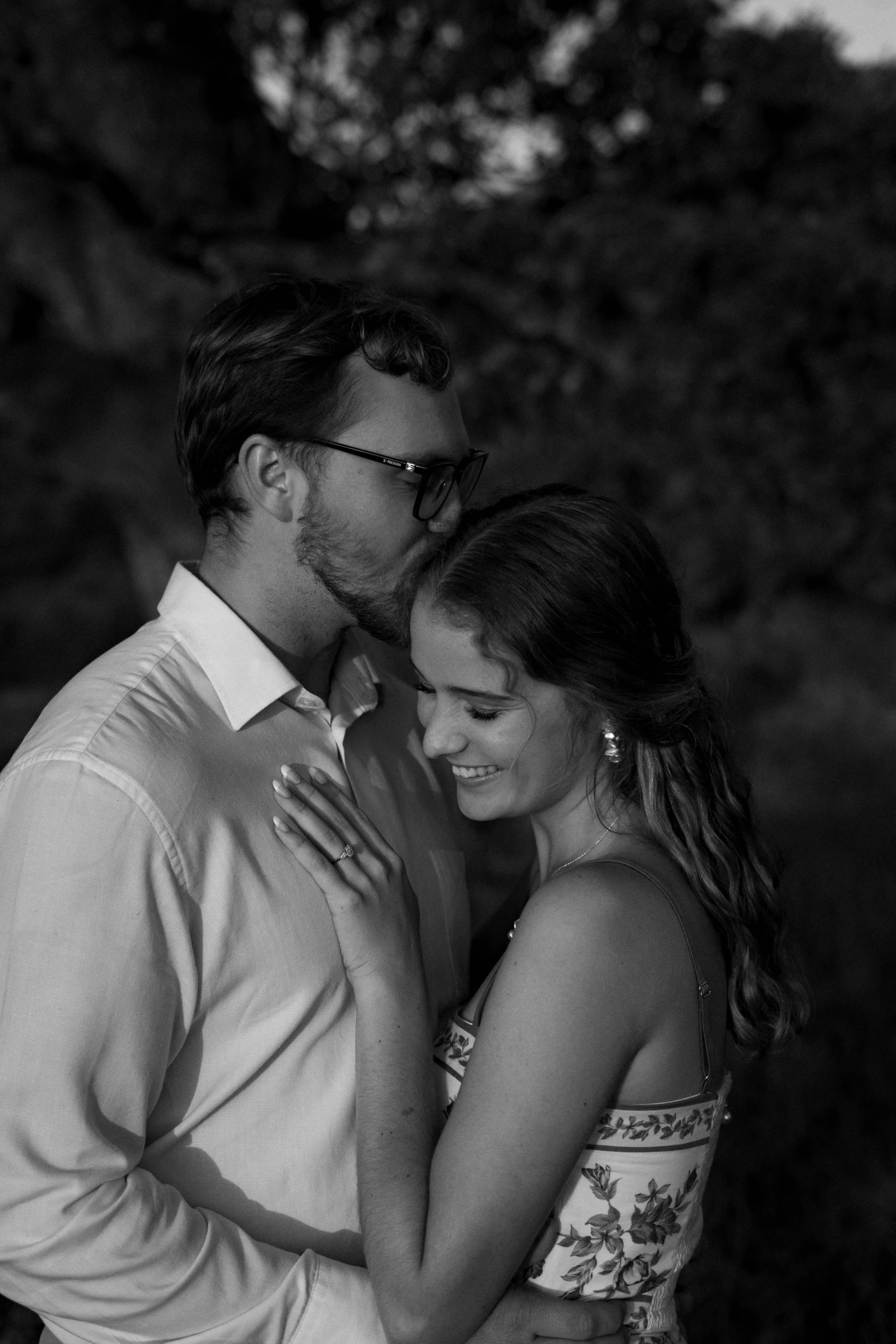 Reinhardt kissing Minke on the forehead as she smiles and shows off her engagement ring, in black and white.